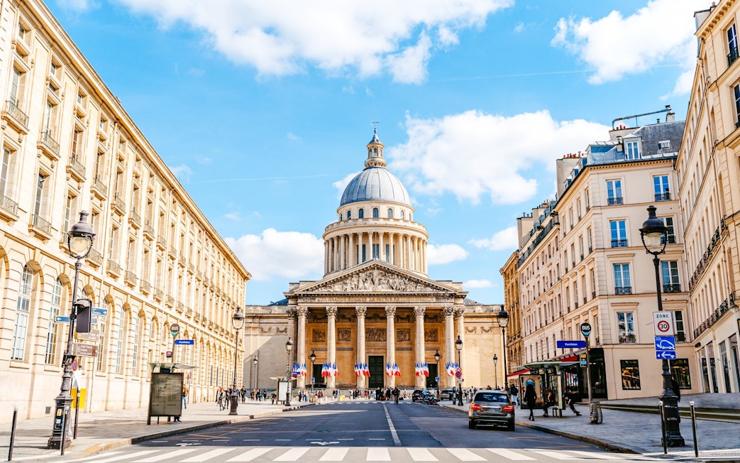 Pantheon in Paris with French flags and surrounding buildings on a sunny day.