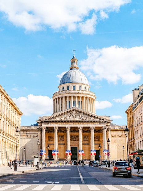 Pantheon in Paris with French flags and surrounding buildings on a sunny day.
