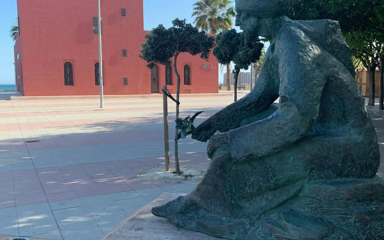 Statue of Don Quixote in Benalmádena near a red building and trees.