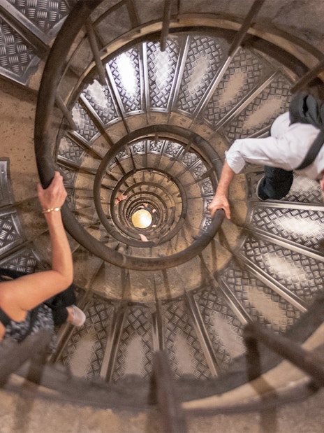 Visitors ascending spiral staircase to Arc de Triomphe rooftop, Paris.