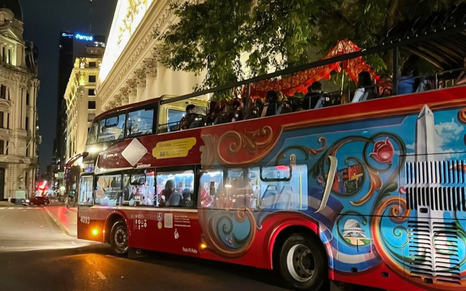 Open-top bus on a night tour in Buenos Aires, passing historic buildings.