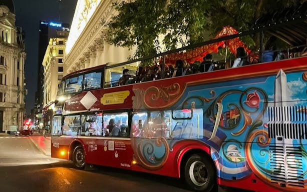 Open-top bus on a night tour in Buenos Aires, passing historic buildings.