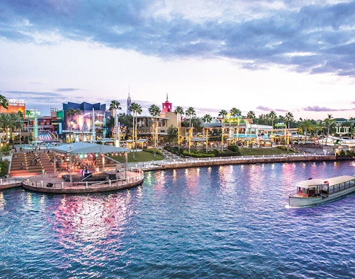 Water taxi on lagoon at Universal Studios Resort, Orlando, Florida, with vibrant cityscape and palm trees.