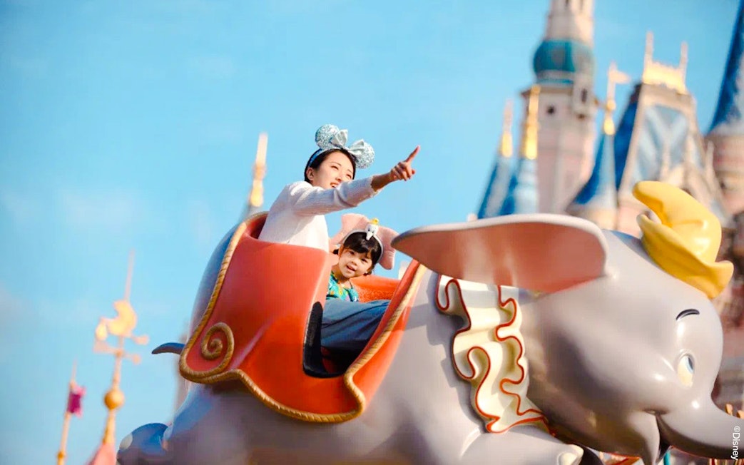 Visitors enjoying Dumbo ride at Shanghai Disney with castle in background.