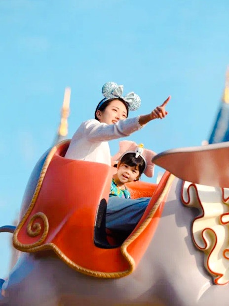 Visitors enjoying Dumbo ride at Shanghai Disney with castle in background.