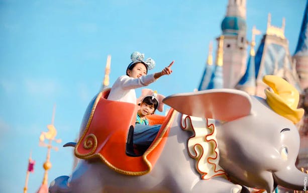 Visitors enjoying Dumbo ride at Shanghai Disney with castle in background.