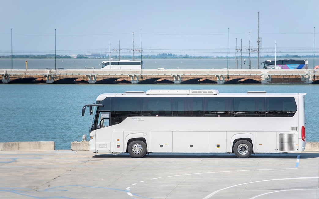 Venice mainland bus parked near water with bridge in background.
