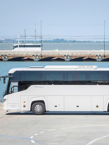 Venice mainland bus parked near water with bridge in background.