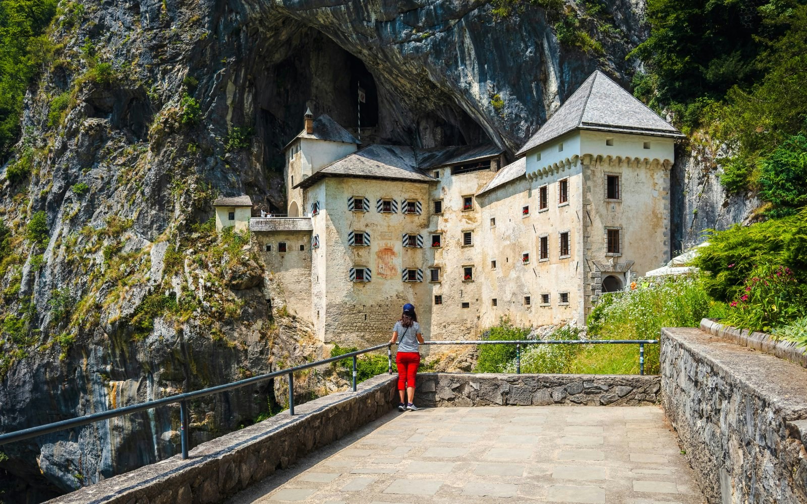 Predjama Castle built into a cliff with a visitor in the foreground, Slovenia.