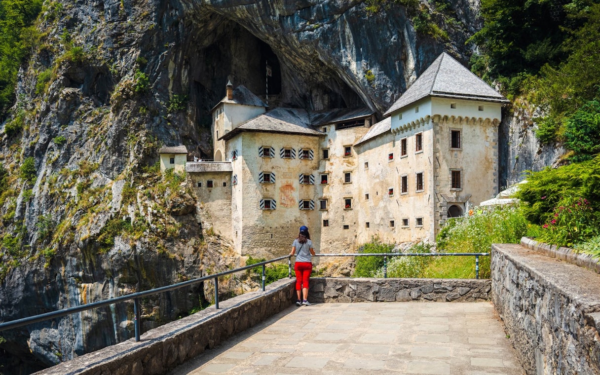 Predjama Castle built into a cliff with a visitor in the foreground, Slovenia.