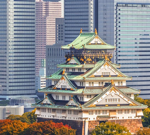 Osaka Castle surrounded by autumn trees with modern skyscrapers in the background.