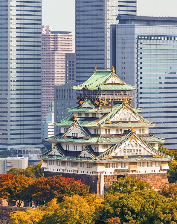 Osaka Castle surrounded by autumn trees with modern skyscrapers in the background.