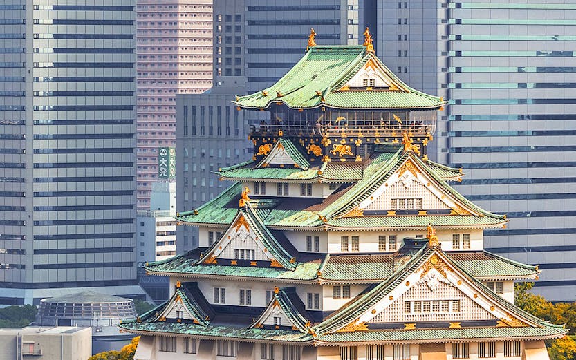 Osaka Castle surrounded by autumn trees with modern skyscrapers in the background.