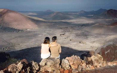 Couple sitting on rocks overlooking Timanfaya Mountains in Lanzarote.