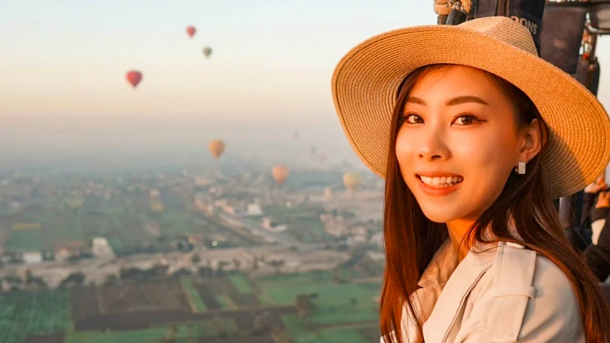 Hot air balloon ride over Luxor landscape with passenger smiling in foreground.