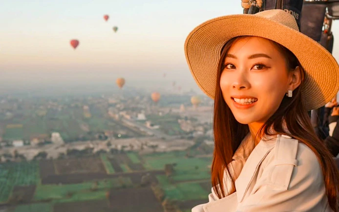 Hot air balloon ride over Luxor landscape with passenger smiling in foreground.