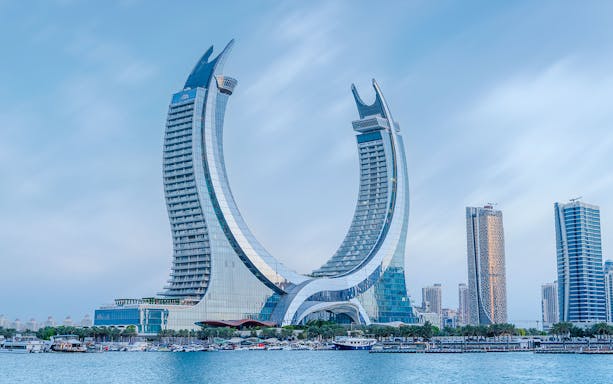 Crescent-shaped skyscraper in Qatar with waterfront view.
