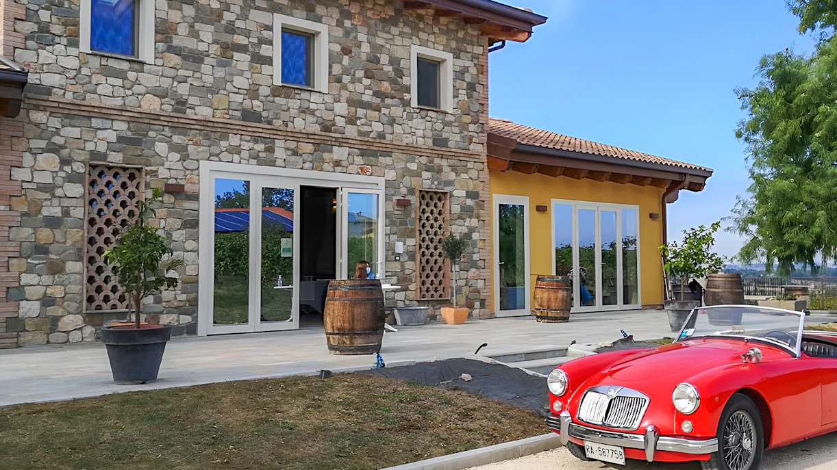Stone farmhouse with barrels and a red vintage car at Acetaia La Vedetta, Modena.