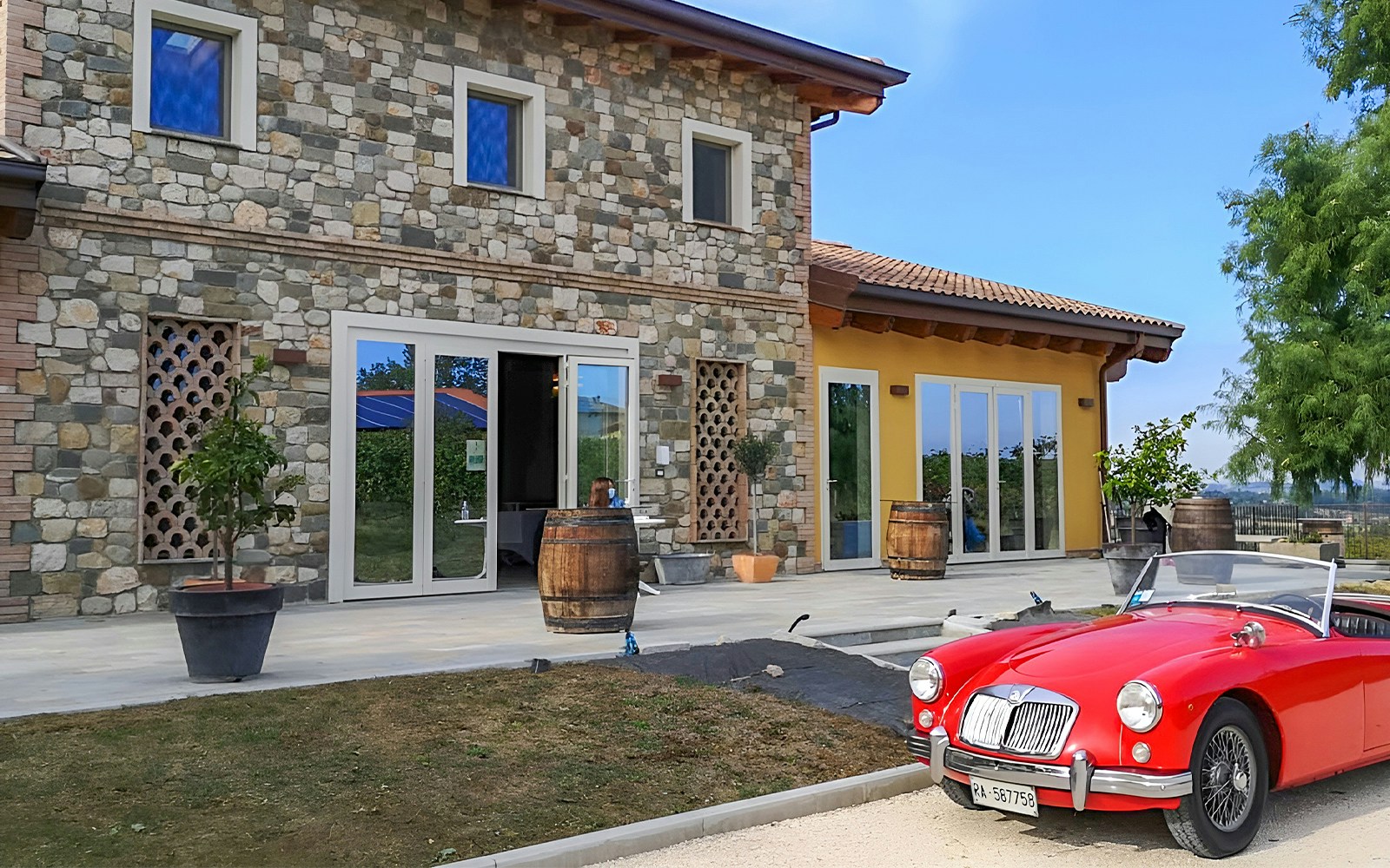 Stone farmhouse with barrels and a red vintage car at Acetaia La Vedetta, Modena.