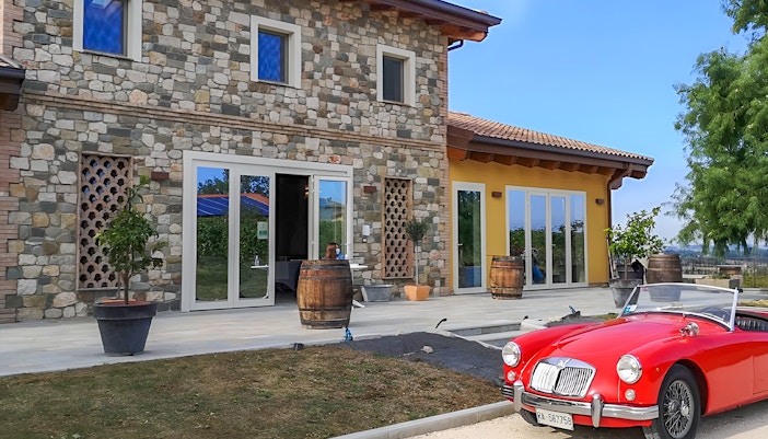 Stone farmhouse with barrels and a red vintage car at Acetaia La Vedetta, Modena.