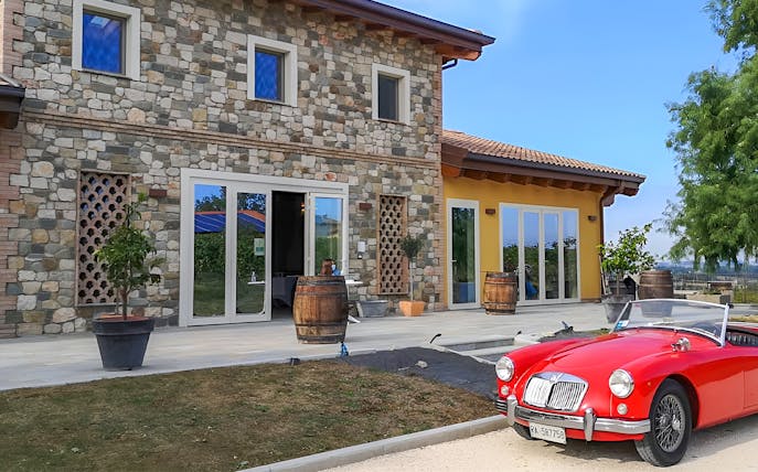 Stone farmhouse with barrels and a red vintage car at Acetaia La Vedetta, Modena.