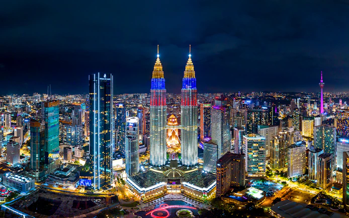 Kuala Lumpur skyline at night featuring the illuminated Petronas Twin Towers.