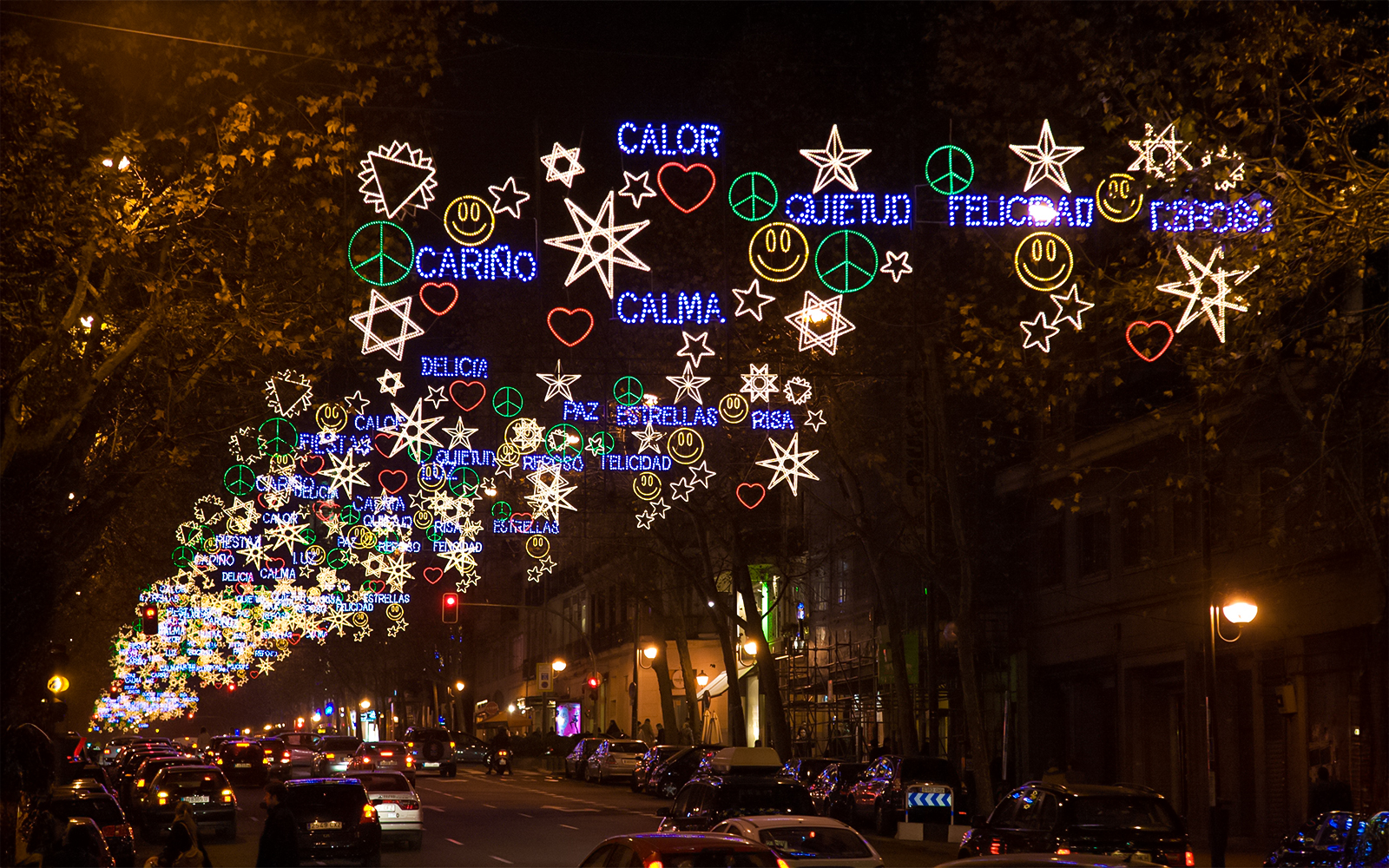 Christmas lights display on a street in Madrid at night, featuring stars and peace symbols.