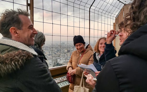 Small group enjoying a guided tour at the Eiffel Tower summit with a view of Paris.