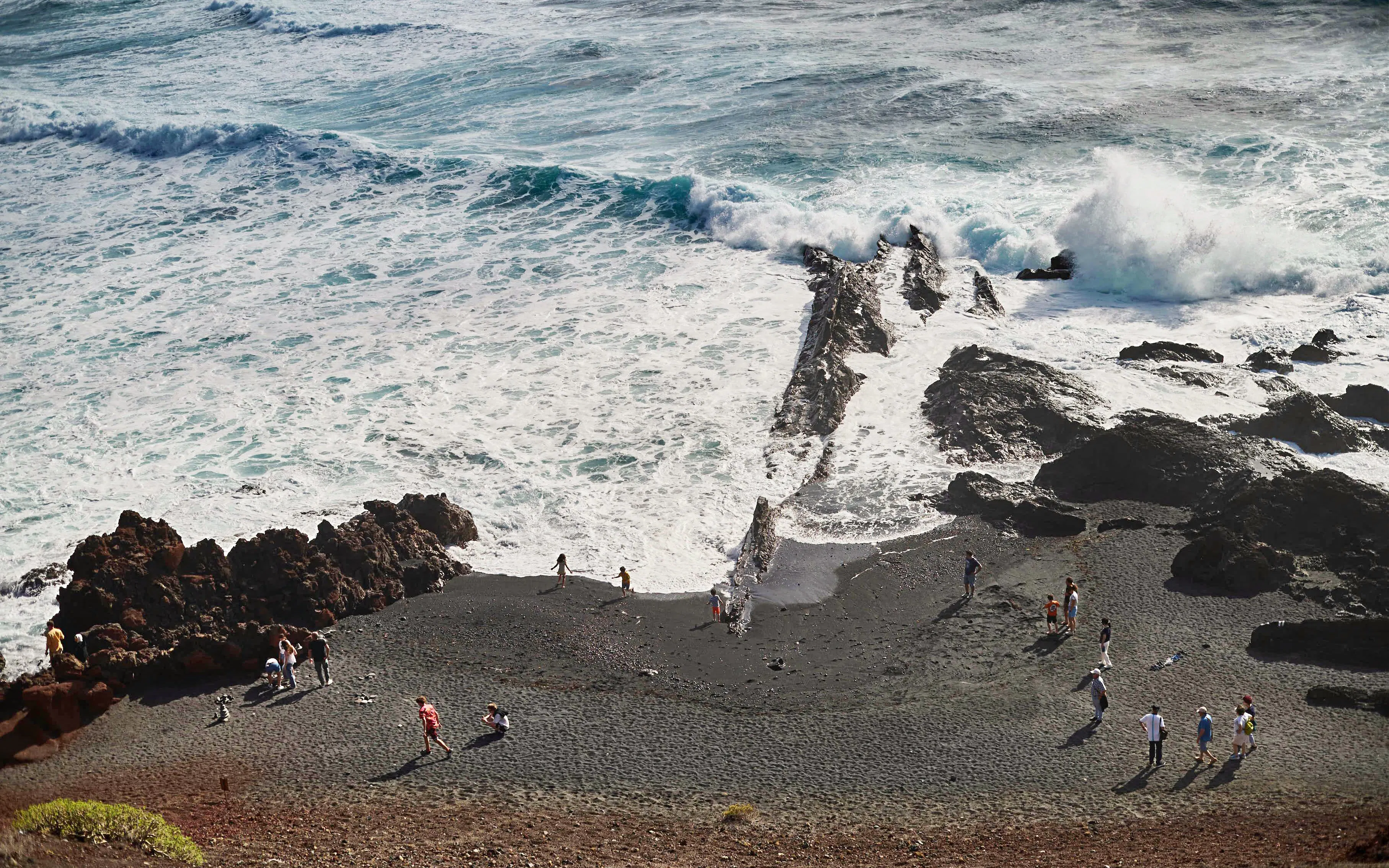 Visitors exploring black sand beach near volcanic rocks, Charco de los Clicos, Lanzarote.