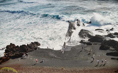 Visitors exploring black sand beach near volcanic rocks, Charco de los Clicos, Lanzarote.