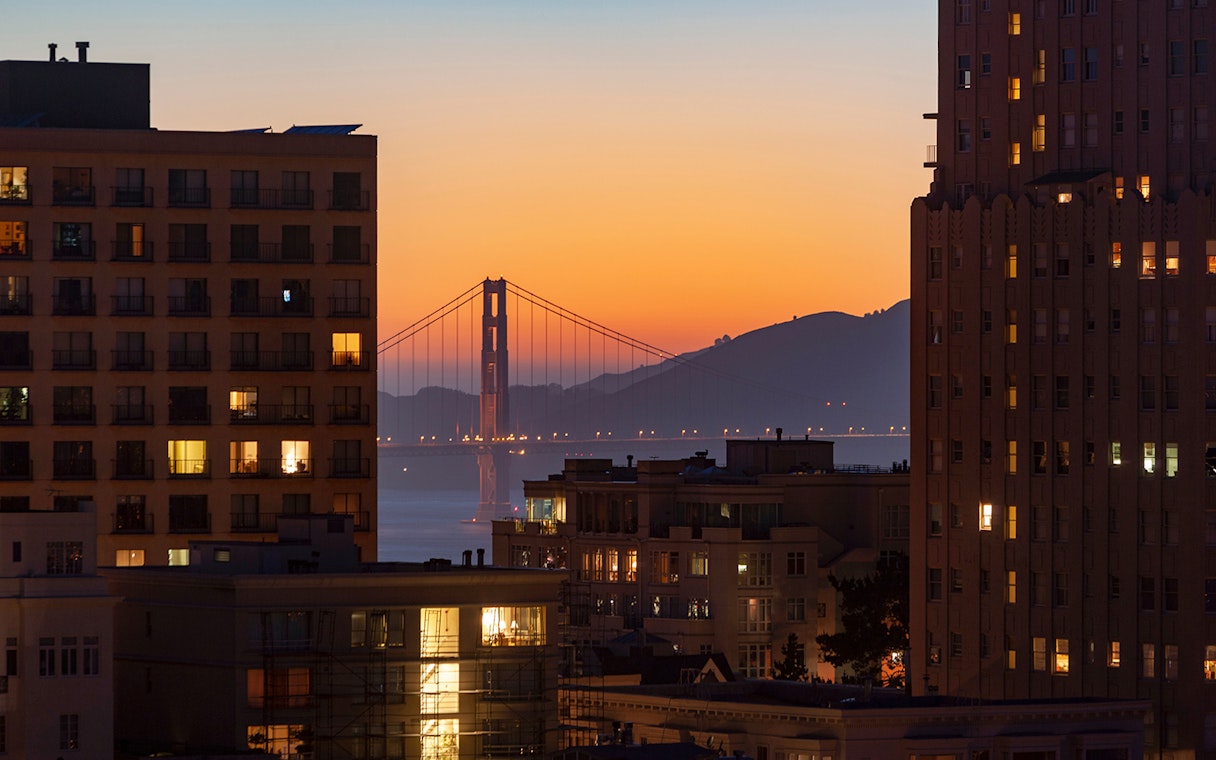 Golden Gate Bridge at sunset viewed between city buildings.