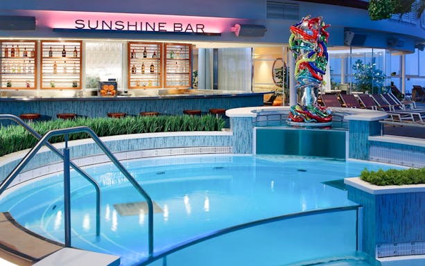 Sunshine Bar on cruise ship with pool and colorful sculpture nearby.