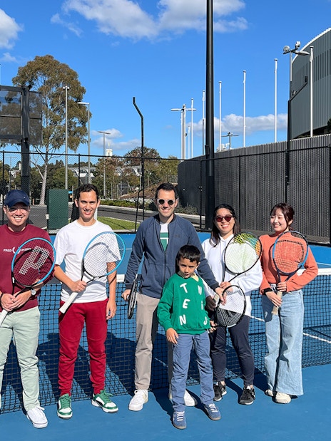 Group holding tennis rackets on court at Melbourne Park during sports walking tour.