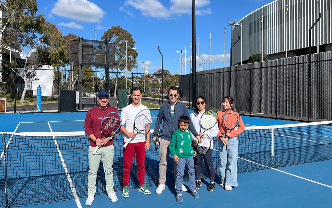 Group holding tennis rackets on court at Melbourne Park during sports walking tour.