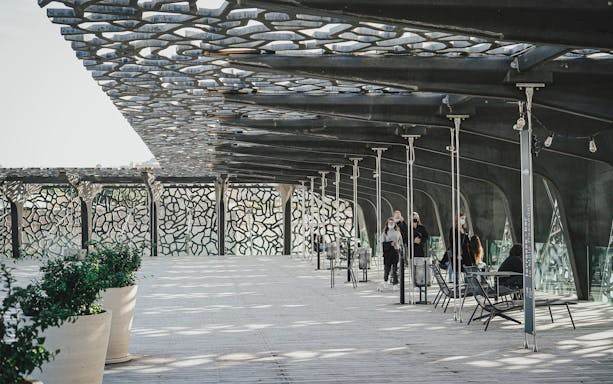 Mucem Marseille terrace with visitors walking under intricate lattice roof.