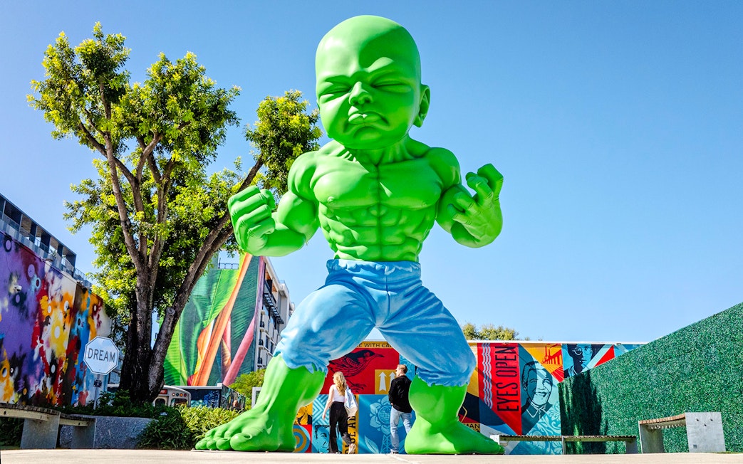 Giant green sculpture at Wynwood Walls Museum with colorful murals in Miami.