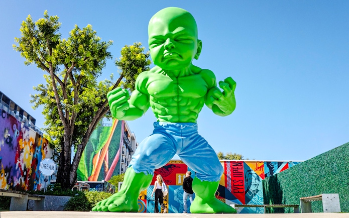 Giant green sculpture at Wynwood Walls Museum with colorful murals in Miami.