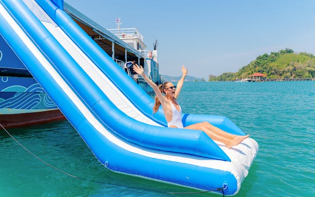 Tourists enjoying an inflatable floating pool slider in a tropical resort setting.