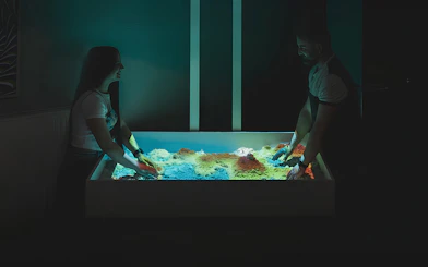 People engaging with interactive sandbox exhibit at DeJa Vu Museum.