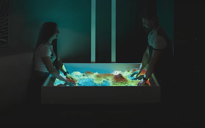 People engaging with interactive sandbox exhibit at DeJa Vu Museum.