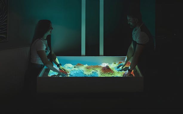 People engaging with interactive sandbox exhibit at DeJa Vu Museum.