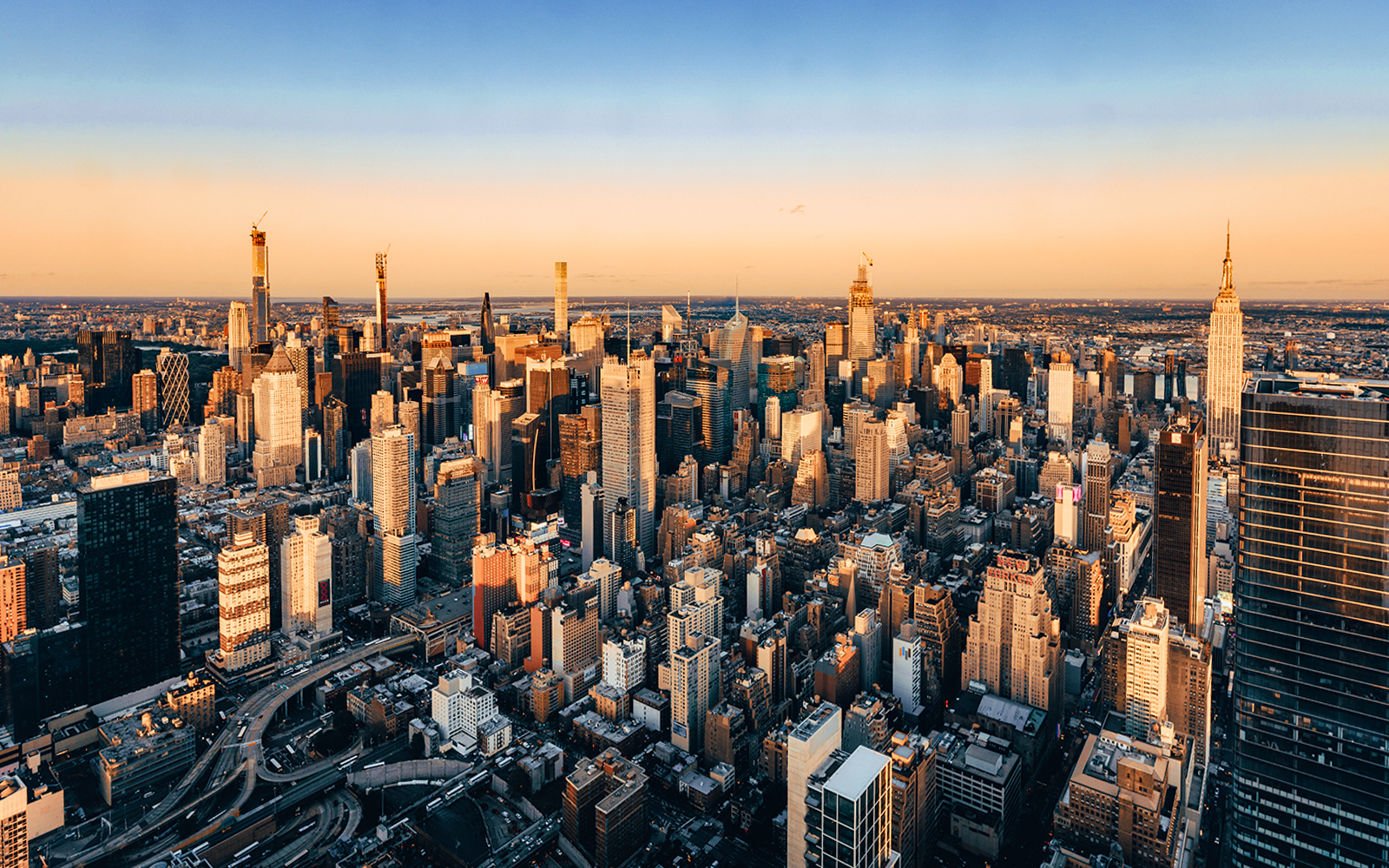 Aerial view of New York City skyline at sunset, featuring skyscrapers and urban landscape.