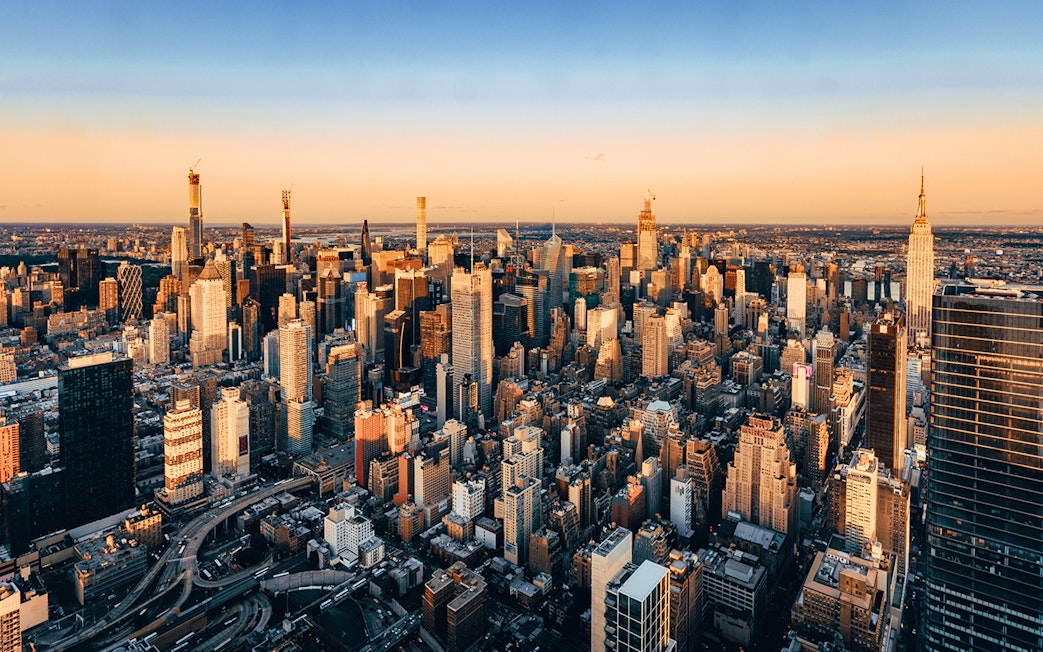 Aerial view of New York City skyline at sunset, featuring skyscrapers and urban landscape.