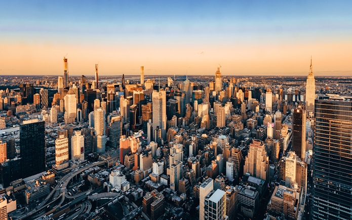 Aerial view of New York City skyline at sunset, featuring skyscrapers and urban landscape.