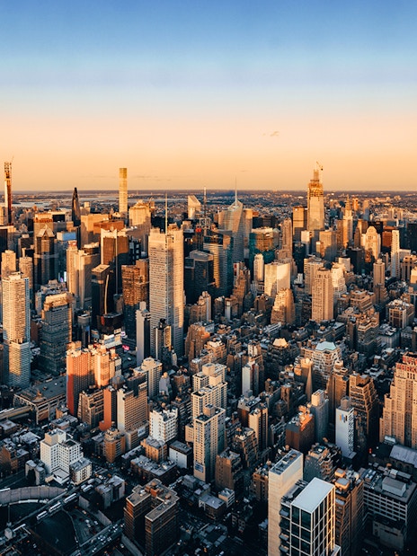 Aerial view of New York City skyline at sunset, featuring skyscrapers and urban landscape.