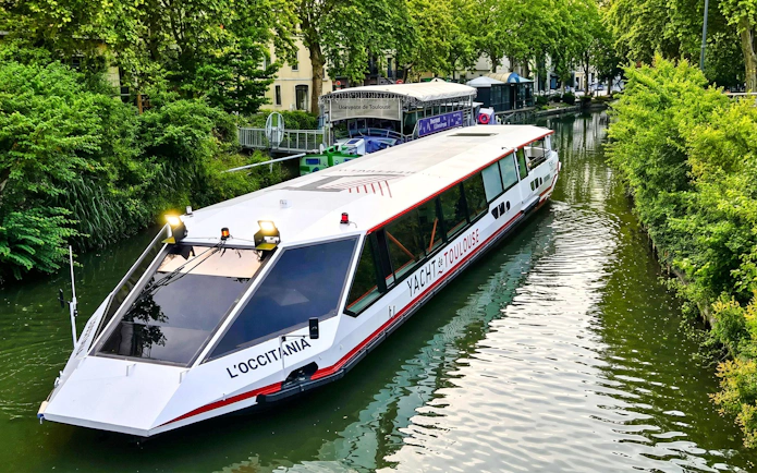 Cruise boat on Canal du Midi in Toulouse with lush greenery and guide commentary.