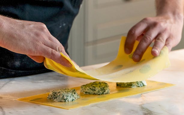 Hands preparing ravioli with spinach filling during a pasta making class.