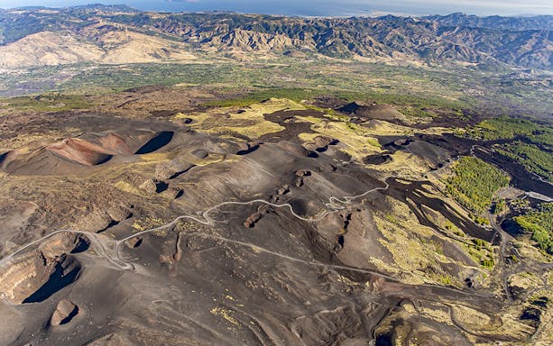 Aerial view of Mount Etna's volcanic landscape with winding roads and craters, Sicily, Italy.