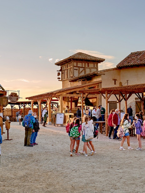 Visitors exploring Puy du Fou España park with rustic buildings and outdoor seating.