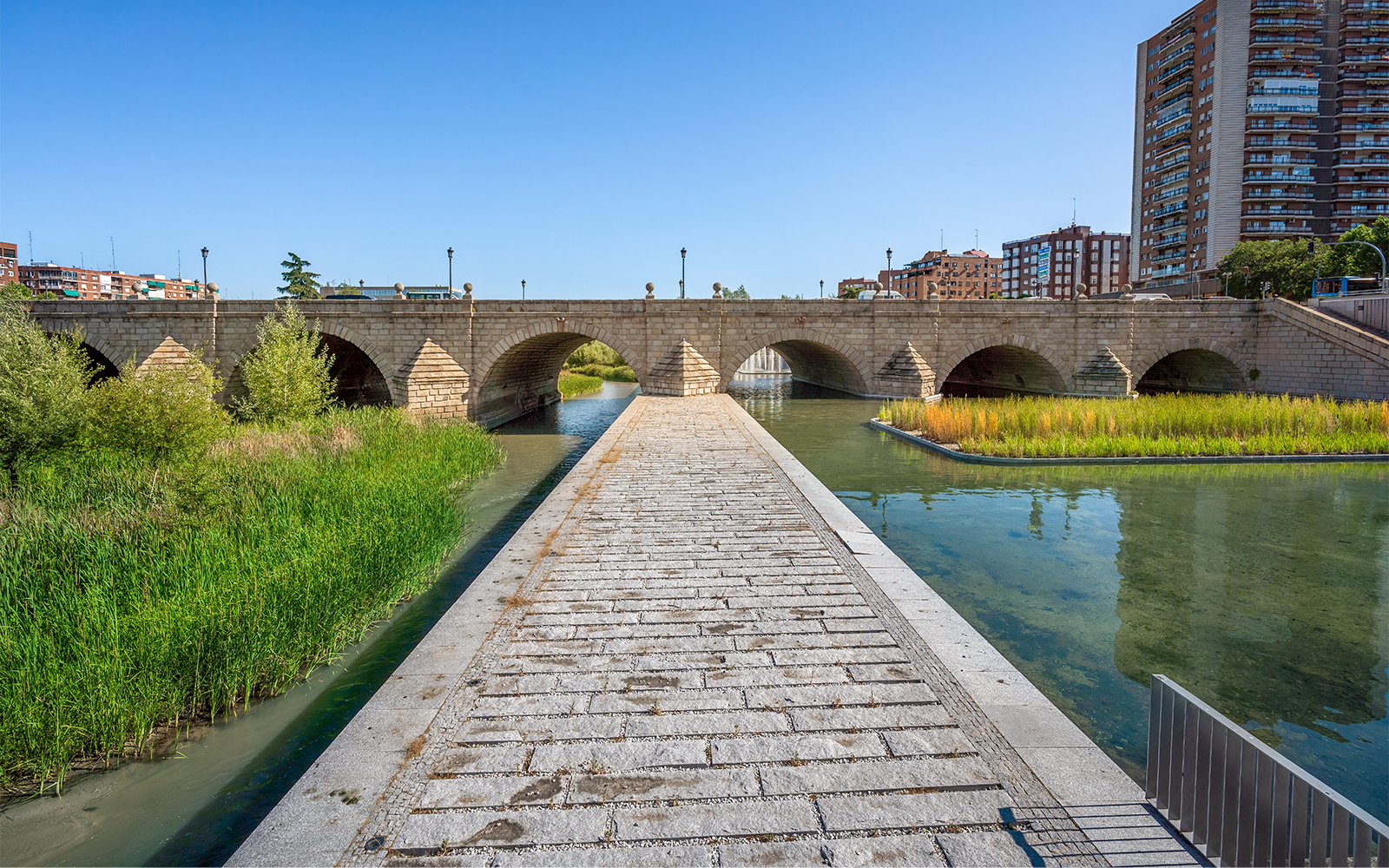 Stone bridge over the Manzanares River in Madrid with surrounding greenery.
